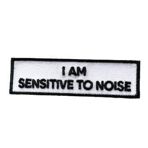 Könnte beinhalten: Weißer rechteckiger Patch mit schwarzem Text, der "I AM SENSITIVE TO NOISE" lautet.