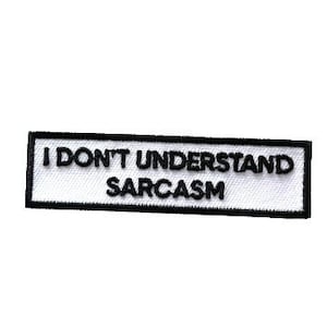 May include: A rectangular white patch with the text "I DON'T UNDERSTAND SARCASTM" in black. The patch has a black border. It is likely an iron-on or sew-on patch for clothing or accessories.