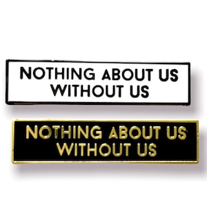 Op de afbeelding: Twee emaille pinnen met de tekst "Nothing About Us Without Us" in zwart en wit. De bovenste pin heeft witte letters op een zwarte achtergrond, en de onderste pin heeft zwarte letters op een witte achtergrond.