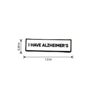 May include: A rectangular white enamel pin with a black border and the black text I HAVE ALZHEIMER'S. The pin measures 1.5 inches in width and 0.39 inches in height as indicated by the black dimension lines and arrows on the sides.