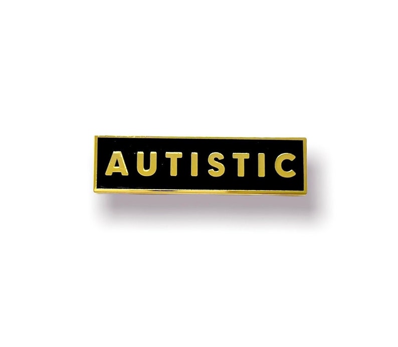 May include: A gold-coloured pin with a black rectangular background. The word "AUTISTIC" is written in gold letters on the pin.