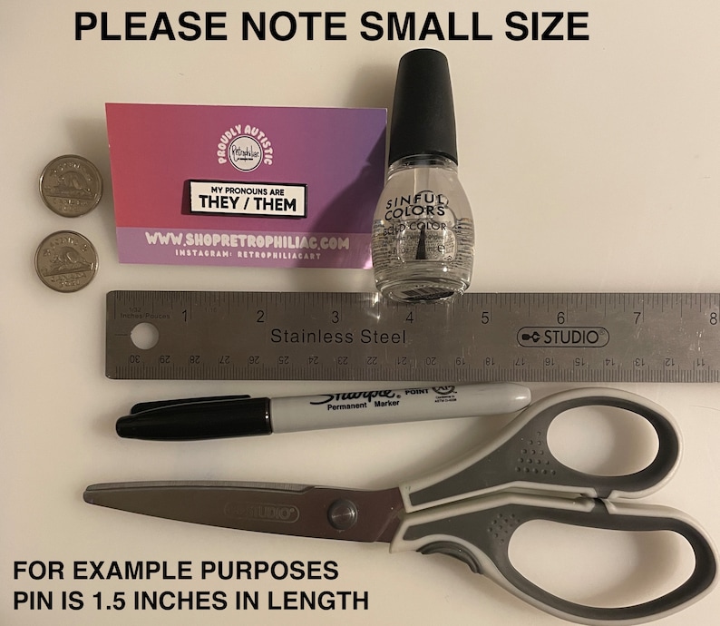Puede incluir: Primer plano de un peque&ntilde;o pin con el texto "My pronouns are they/them" sobre un fondo rosa y blanco. El pin est&aacute; al lado de una regla, un marcador negro, unas tijeras y una botella de esmalte de u&ntilde;as transparente. El texto "Please note small size" est&aacute; en la parte superior de la imagen. El texto "For example purposes pin is 1.5 inches in length" est&aacute; en la parte inferior de la imagen.