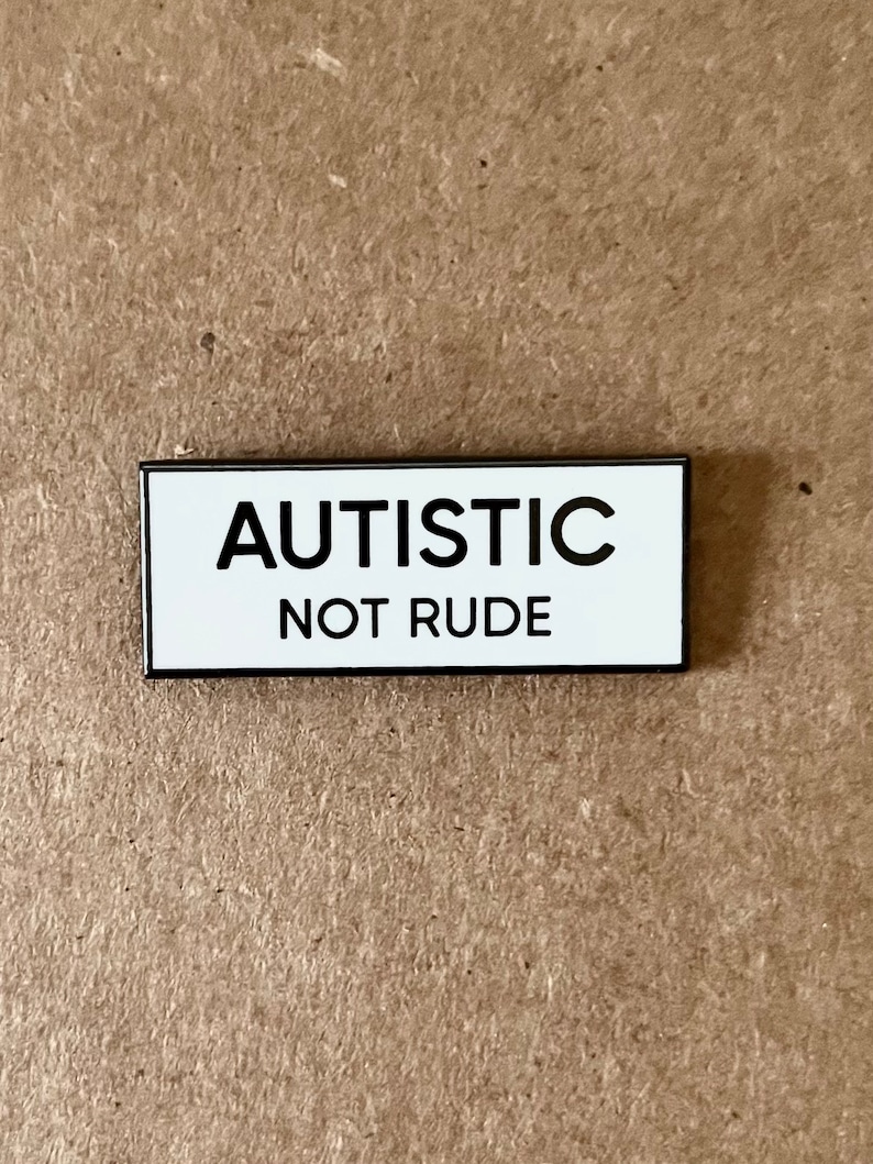 May include: White enamel pin with black lettering that reads "Autistic Not Rude".