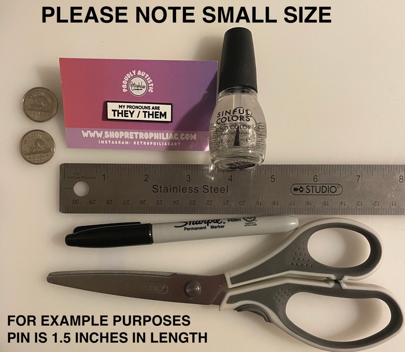 May include: A close-up of a small pin with the text "My pronouns are they/them" on a pink and white background. The pin is next to a ruler, a black marker, a pair of scissors, and a bottle of clear nail polish. The text "Please note small size" is at the top of the image. The text "For example purposes pin is 1.5 inches in length" is at the bottom of the image.