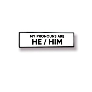 May include: Black and white enamel pin with the text "My pronouns are He/Him".