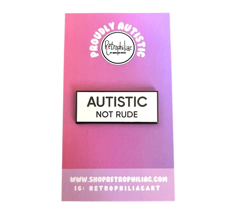 May include: White enamel pin with black text that reads "Autistic Not Rude". The pin is on a pink and white background with the text "Proudly Autistic" in a circle.