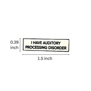 May include: A rectangular pin with a white background and a black border. The text reads I HAVE AUDITORY PROCESSING DISORDER in black capital letters. The pin measures 1.5 inches in length and 0.39 inches in height as indicated by the markings.