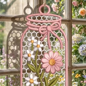 May include: A hanging wall decoration shaped like a mason jar, featuring pink embroidered outlines, a pink bow, and a white honeycomb mesh background. The design includes embroidered white and pink flowers with green stems and yellow centres.