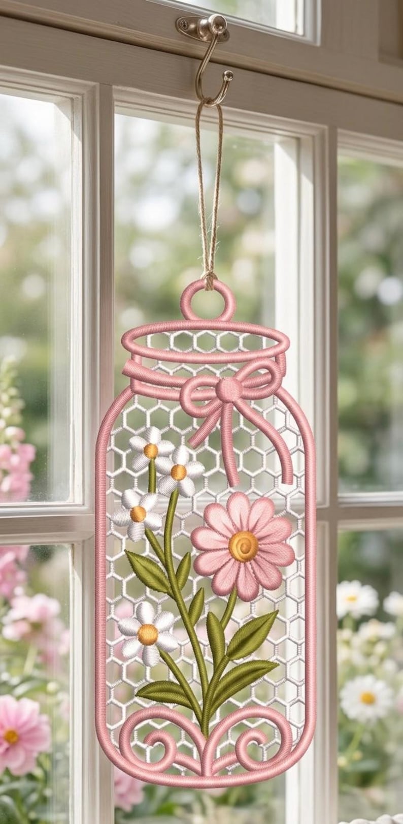 May include: A hanging embroidered decoration shaped like a mason jar with a pink border and a white honeycomb mesh background. It features stitched white daisies with yellow centres and a large pink flower, accented by a pink bow at the top.