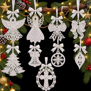 Puede incluir: Una colección de adornos colgantes blancos cortados con láser que presentan varias formas, incluyendo un ángel, un árbol de Navidad, una campana, un copo de nieve, una cruz y lazos. Cada adorno está suspendido por una cinta blanca atada.