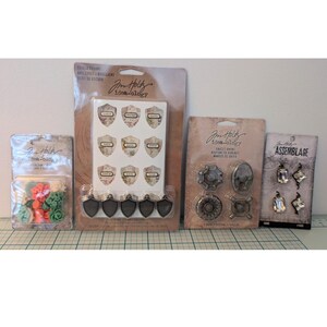 Peut inclure: Quatre paquets de fournitures de loisirs créatifs Tim Holtz Idea-ology. L'ensemble comprend de petites décorations florales colorées, des breloques en forme de bouclier avec du texte, des boutons de robinet métalliques et des breloques en cristal.
