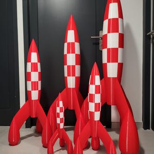 Peut inclure: Collection de cinq fusées jouets rouges et blanches. Les corps des fusées sont rouges avec des motifs à carreaux blancs. Chaque fusée a trois pieds rouges. Les fusées varient en taille, la plus grande étant la plus haute.