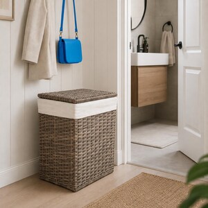 Peut inclure: Un panier à linge rectangulaire en matériau synthétique tressé gris, doté d'une doublure en tissu blanc amovible et d'un couvercle assorti. Le panier présente une structure rigide et est placé dans une pièce aux murs et sols clairs.