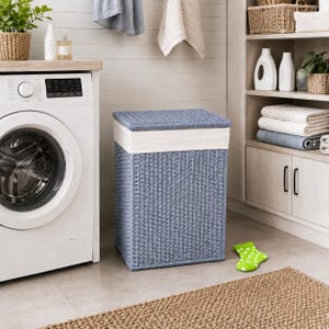 Peut inclure: Un panier à linge rectangulaire doté d'un extérieur en matière synthétique tressée bleue et d'une bande de tissu blanc uni près du sommet. Le panier présente un couvercle bleu assorti et une structure rigide, posé sur le sol près d'un lave-linge.