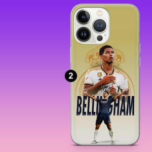 May include: A gold-toned smartphone case featuring a graphic of Jude Bellingham. The design includes a large portrait of the athlete in a white jersey, a smaller full-body image in a dark blue kit, a crown emblem, and the text BELLINGHAM in bold.