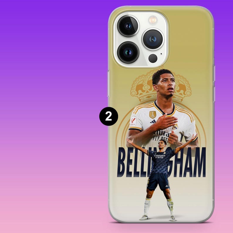 May include: A gold-toned smartphone case featuring a graphic of Jude Bellingham. The design includes a large portrait of the athlete in a white jersey, a smaller full-body image in a dark blue kit, a crown emblem, and the text BELLINGHAM in bold.