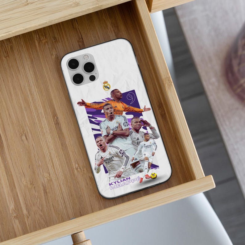 K&ouml;nnte beinhalten: Eine wei&szlig;e Smartphone-H&uuml;lle mit einer Collage von Kylian Mbapp&eacute; in Real Madrid Fu&szlig;balltrikots. Das Design zeigt den Spieler in verschiedenen Posen, die Nummer 9, das Real Madrid Wappen und den Text KYLIAN MBAPP&Eacute; am unteren Rand der H&uuml;lle.