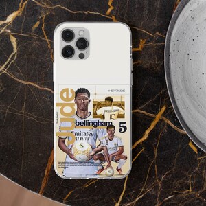 May include: A clear phone case featuring a collage of Jude Bellingham in a white Real Madrid jersey. The design includes the text "Jude", "Bellingham", "#HEYJUDE", and the number "5". The player is shown holding a football in two poses.