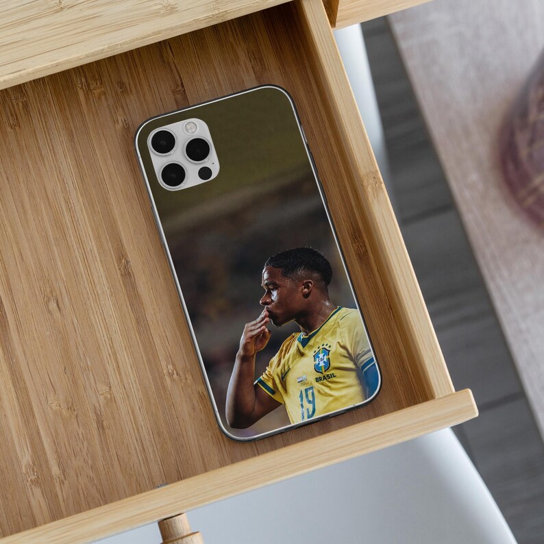 May include: A smartphone case featuring a printed image of a soccer player wearing a yellow Brazil national team jersey with the number 19 visible. The player is shown in profile, touching their lips with their fingers in a celebratory gesture.
