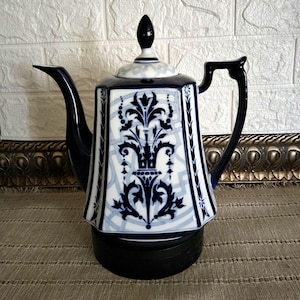 May include: A hexagonal porcelain teapot featuring a white base with a dark blue floral pattern and a geometric light blue background. The teapot has a dark blue handle, a matching dark blue spout, and a lid topped with a dark blue finial.