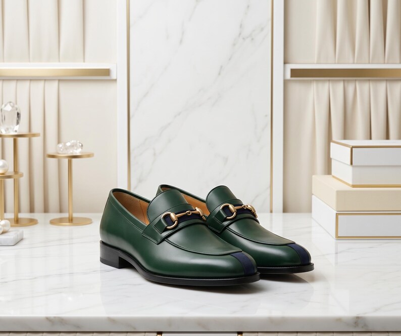 May include: A pair of dark green leather loafers featuring a gold-toned metal horsebit detail across the vamp and a navy blue vertical stripe accent on the toe. The shoes have a low black heel and a smooth, polished finish on the exterior leather.