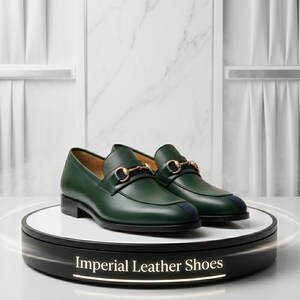May include: A pair of dark green leather loafers featuring a gold-toned metal horsebit detail across the vamp and a dark blue stripe accent on the toe. The shoes are displayed on a circular stand with the text Imperial Leather Shoes printed on it.
