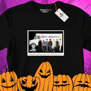 May include: A black t-shirt featuring a graphic print of a white truck labelled DIE-NAMITE with seven figures in costumes standing in front of it. Below the truck, the text reads, Shining through the graveyard with a little funk and soul.