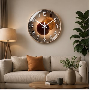 May include: A round wall clock with a metallic gold frame and a dark brown face featuring a celestial design of two overlapping planets. The clock has white Arabic numerals from 1 to 12 and thin white hour, minute, and second hands.