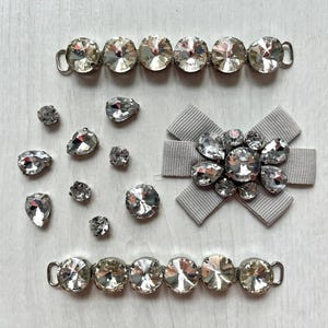 May include: A collection of clear crystal embellishments including two long metal-linked chains of round faceted stones, a grey ribbon bow centred with a cluster of clear crystals, and several loose teardrop and round faceted crystal stones.