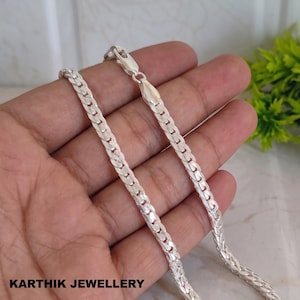 Puede incluir: Un collar de cadena de plata con un diseño de eslabones planos entrelazados, acabado pulido y un cierre de mosquetón seguro. El texto KARTHIK JEWELLERY está impreso en negro en la esquina inferior izquierda de la imagen.