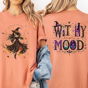 May include: A terracotta-colored t-shirt featuring a front graphic of a witch in a black dress with the text Spellbound & Unbothered and a back graphic with the text WITCHY MOOD, surrounded by illustrations of a hat, cat, moon, and potions.