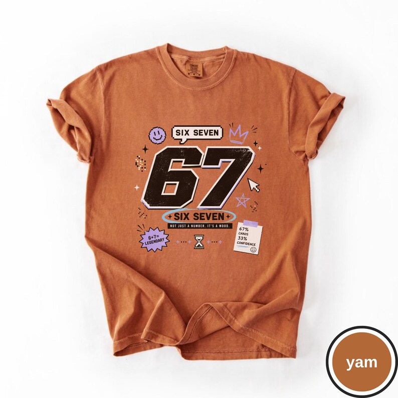 Pu&ograve; includere: Una t-shirt color ruggine con una grande grafica nera del numero 67 e il testo SIX SEVEN, NOT JUST A NUMBER. IT'S A MOOD. Include grafiche di una faccina sorridente, corona, clessidra, stella, cursore e una nota 67% CHAOS 33% CONFIDENCE.