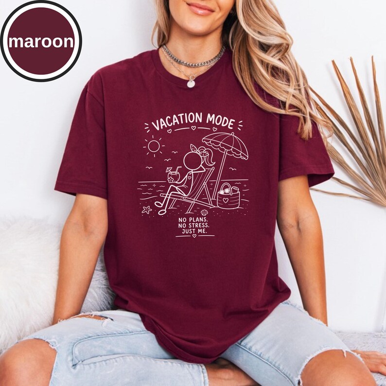 May include: Maroon t-shirt with a white graphic of a person relaxing on a beach chair under an umbrella. The text "VACATION MODE" and "NO PLANS. NO STRESS. JUST ME." are also printed on the shirt.