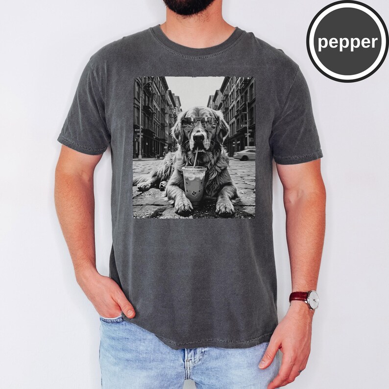 Peut inclure: Un t-shirt &agrave; col rond gris anthracite avec une impression graphique en noir et blanc repr&eacute;sentant un chien portant des lunettes de soleil et buvant dans un gobelet en plastique avec une paille, sur fond de rue urbaine. Le mot pepper est inscrit.