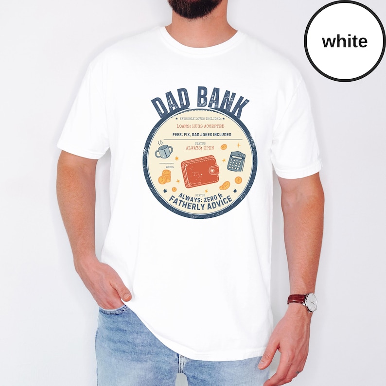 May include: White t-shirt with a circular graphic that reads "DAD BANK" in blue. The graphic includes a wallet, calculator, coffee cup, and coins. The text "ALWAYS: ZERO & FATHERLY ADVICE" is also included.