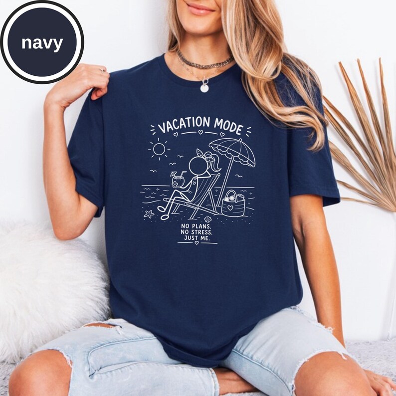 May include: Navy blue t-shirt with a white graphic of a person relaxing on a beach chair under an umbrella. The text "VACATION MODE" and "NO PLANS. NO STRESS. JUST ME." are also printed on the shirt.