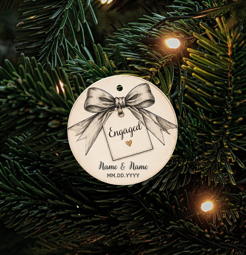 May include: A round white ornament featuring a black and white illustration of a bow tied to a gift tag. The tag displays the text Engaged with a small gold heart. Below the tag, the text Name & Name and MM.DD.YYYY is printed in black ink.