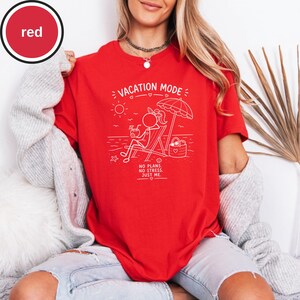 May include: A red t-shirt with a white graphic of a person relaxing on a beach chair under an umbrella. The text "VACATION MODE" and "NO PLANS. NO STRESS. JUST ME." are also printed on the shirt.