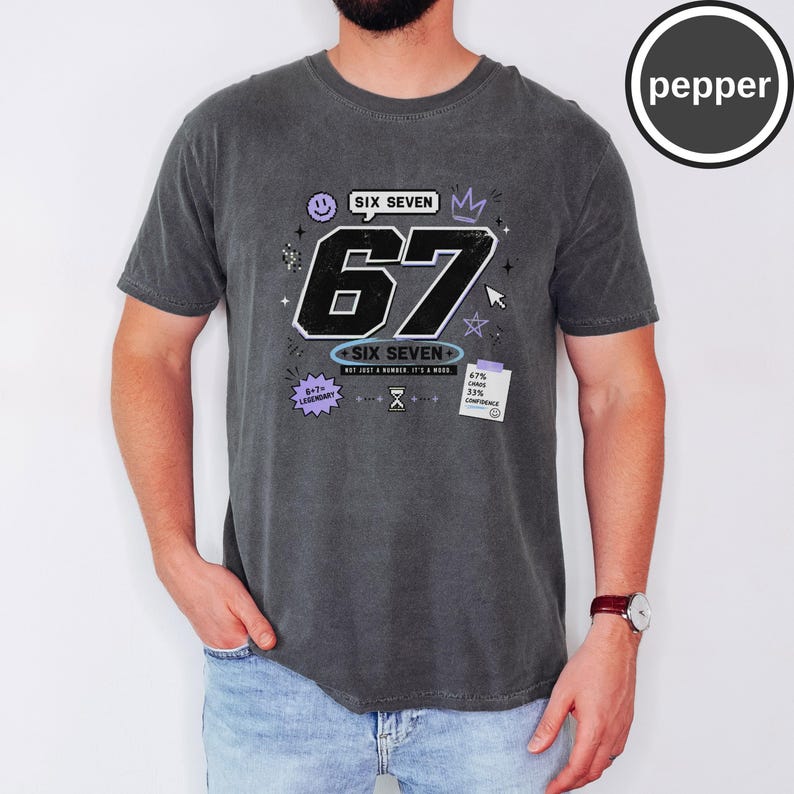 Pu&ograve; includere: Una t-shirt a maniche corte grigio antracite con una stampa grafica che presenta il grande numero 67, il testo SIX SEVEN e piccoli elementi decorativi tra cui una faccina sorridente, una corona, stelle e una nota con 67% chaos 33% confidence.
