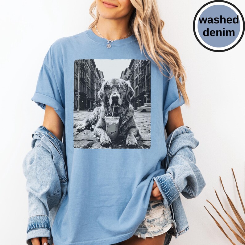 Peut inclure: Un t-shirt bleu denim d&eacute;lav&eacute; avec une impression graphique en noir et blanc repr&eacute;sentant un chien portant des lunettes de soleil et buvant dans un gobelet avec une paille dans une rue. Le texte "washed denim" figure dans un badge circulaire.