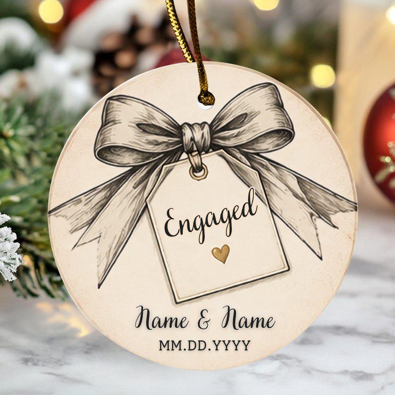 May include: A round ceramic ornament featuring a sketch-style illustration of a large bow tied to a rectangular gift tag. The tag displays the word Engaged with a small gold heart. Below, the text Name & Name and MM.DD.YYYY is printed.