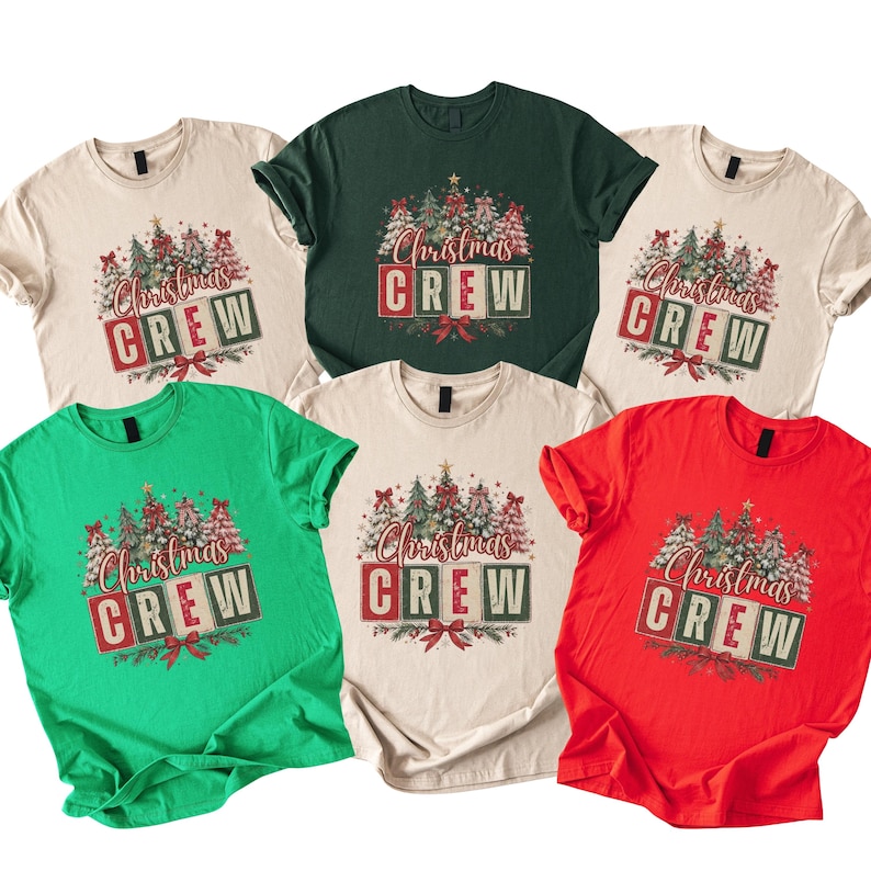 Op de afbeelding: Een collectie van zes t-shirts met korte mouwen in beige, donkergroen, felgroen en rood. Elk shirt heeft een grafische print van kerstbomen en de tekst "Christmas CREW" op blokken met een rode strik aan de onderkant.