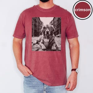 Peut inclure: Un t-shirt &agrave; manches courtes couleur cramoisi avec une impression graphique rectangulaire en noir et blanc repr&eacute;sentant un chien portant des lunettes de soleil et buvant dans un gobelet en plastique avec une paille dans une rue. Le mot crimson est encercl&eacute;.