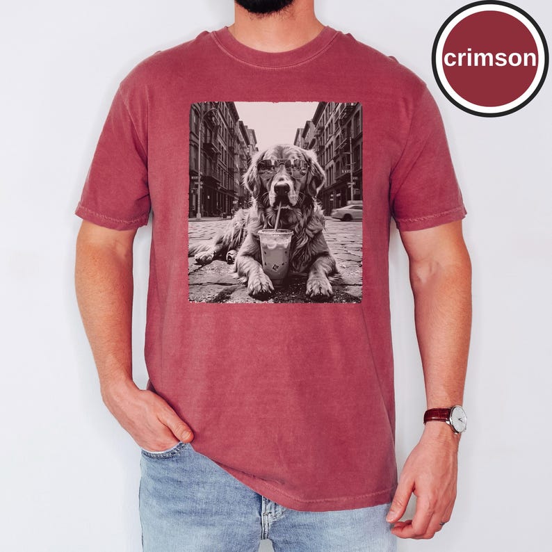Peut inclure: Un t-shirt &agrave; manches courtes couleur cramoisi avec une impression graphique rectangulaire en noir et blanc repr&eacute;sentant un chien portant des lunettes de soleil et buvant dans un gobelet en plastique avec une paille dans une rue. Le mot crimson est encercl&eacute;.