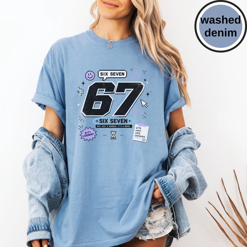Pu&ograve; includere: Una t-shirt a maniche corte in blu denim slavato con una grande grafica nera del numero 67, il testo SIX SEVEN, una faccina sorridente, un'icona a clessidra e una nota con scritto 67 CHAOS 33 CONFIDENCE, oltre al testo 6+7 LEGENDARY.