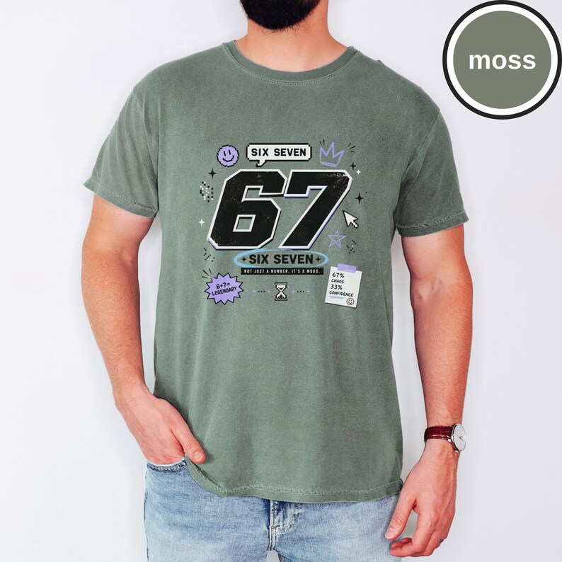 Pu&ograve; includere: Una t-shirt a maniche corte color verde muschio con una stampa grafica che presenta il grande numero nero 67, il testo SIX SEVEN e varie piccole icone tra cui una faccina sorridente, una corona, una clessidra e una nota con 67% CHAOS 33% CONFIDENCE.