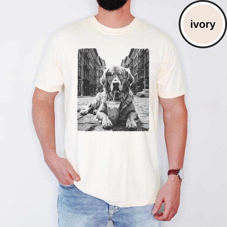 Peut inclure: Un t-shirt ivoire &agrave; manches courtes avec une impression graphique en noir et blanc repr&eacute;sentant un chien portant des lunettes de soleil et buvant dans un gobelet en plastique avec une paille, sur fond de rue urbaine. Col rond et coupe d&eacute;contract&eacute;e.