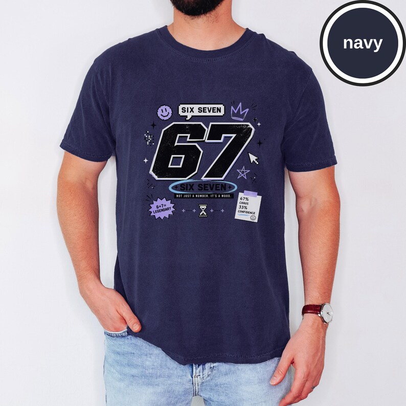 Pu&ograve; includere: Una t-shirt blu navy a maniche corte con una grande grafica del numero 67 in nero con contorni bianchi. Il design include piccole icone come una faccina sorridente, una corona, una stella, una clessidra e il testo SIX SEVEN, NOT JUST A NUMBER, IT'S A MOOD.