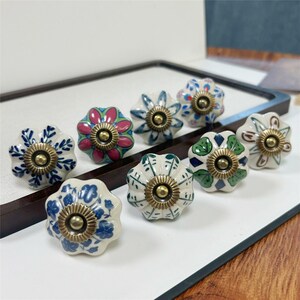 Peut inclure: Ensemble de huit boutons de meuble en céramique en forme de fleur. Chaque bouton présente un motif floral unique dans diverses couleurs, dont le bleu, le rose, le vert et le blanc, avec un centre de couleur laiton. Ces boutons décoratifs sont parfaits pour ajouter une touche d'élégance aux meubles.