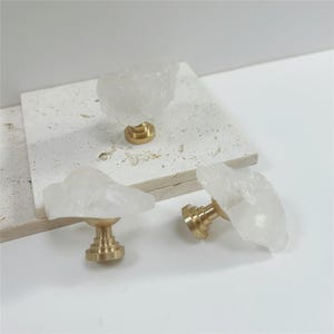 Peut inclure: Ensemble de trois boutons de meuble en cristal de quartz clair avec quincaillerie en laiton. Les boutons ont une forme naturelle et irrégulière et sont montés sur une base en laiton. Présentés sur une surface blanche.